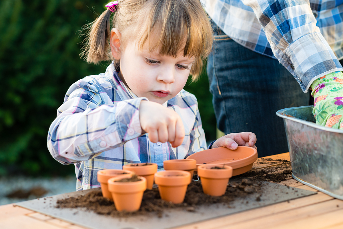 Girl planting flower seeds into pots with her mother